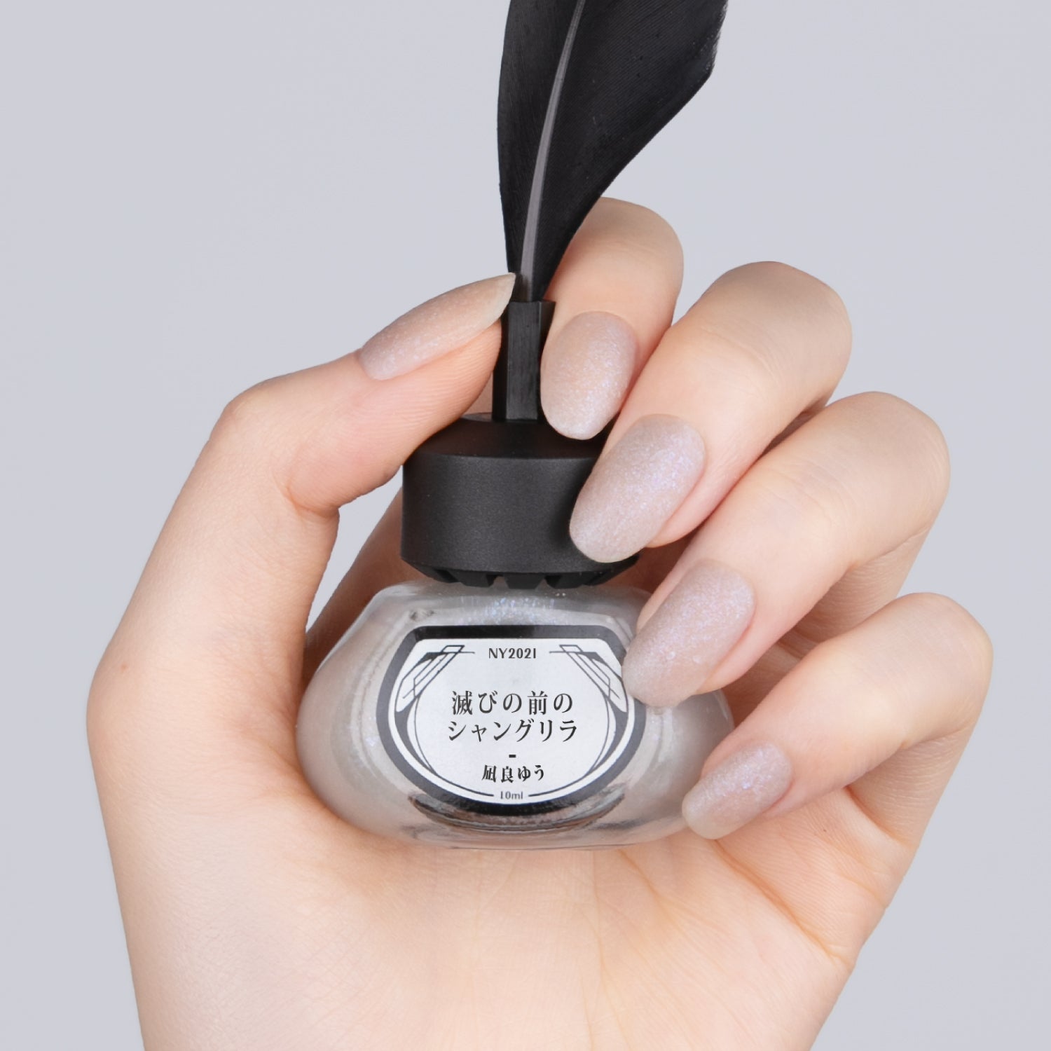 NY2021 滅びの前のシャングリラ【8/25正午発売】 - et seq.(エセク)羽根ペンネイルポリッシュ - マニキュア
淡いシルバーラメ×マットのネイルを塗った手が、黒い羽根ペン付きのインク瓶型ネイルポリッシュを持っている。ラベルには『滅びの前のシャングリラ 凪良ゆう』と記載。