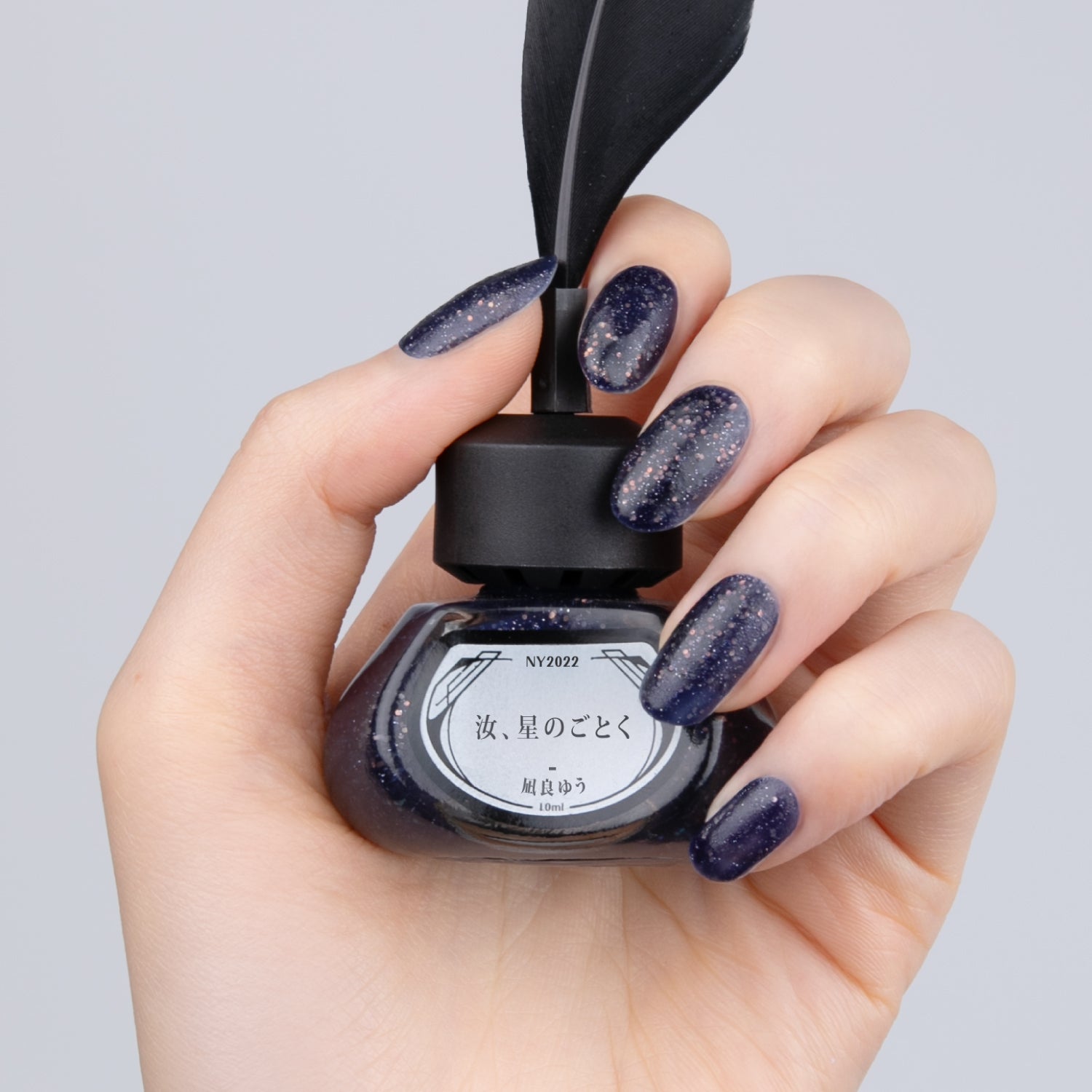 NY2022 汝、星のごとく【8/25正午発売】 - et seq.(エセク)羽根ペンネイルポリッシュ - マニキュア
少し紫がかった紺色のラメ×マットのネイルを塗った手が、
黒い羽根ペン付きのインク瓶型ネイルポリッシュを持っている。ラベルには『汝、星のごとく 凪良ゆう』と記載。